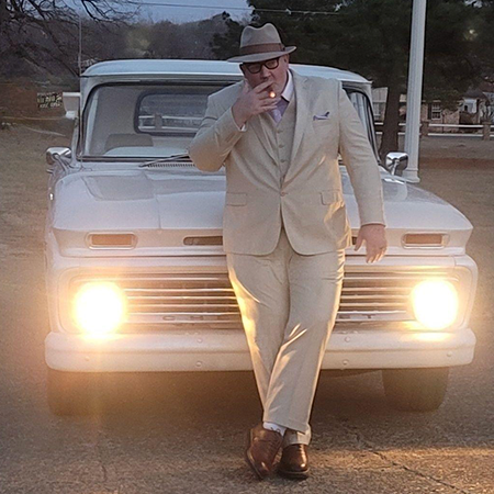 Uncle Ryano standing in the front of a classic white truck smoking a cigar.